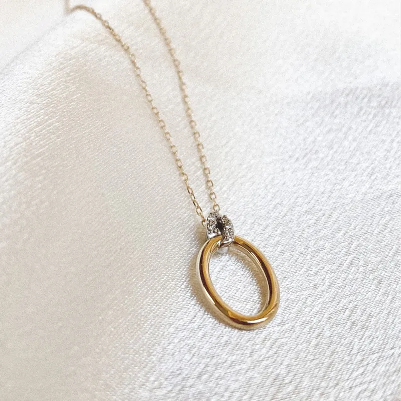 Gold and silver necklace with an oval pendant, displayed on a soft fabric background.