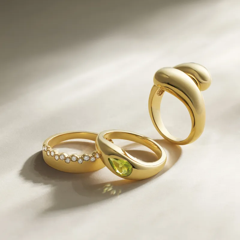 Three elegant gold rings: one with diamonds, one with a green gemstone, and a smooth twisted design.