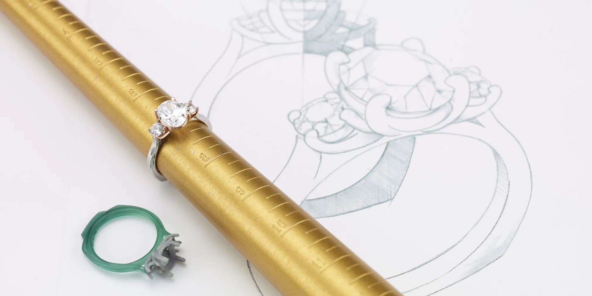 Engagement ring on a gold ring mandrel with a sketch of the design and a wax model beside it. Click to start a project.