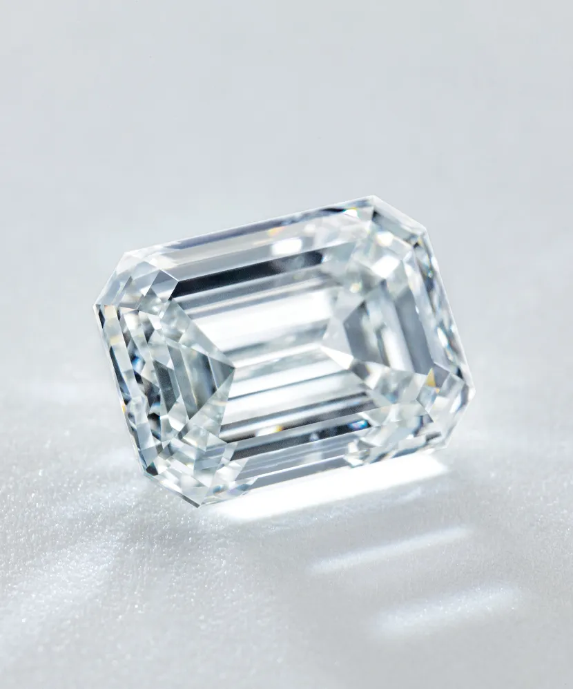 Clear emerald-cut diamond resting on a light surface, showcasing its brilliance and clarity.