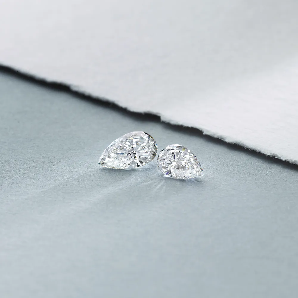 Two sparkling pear-shaped diamonds on a soft gray surface, showcasing their brilliance and clarity.