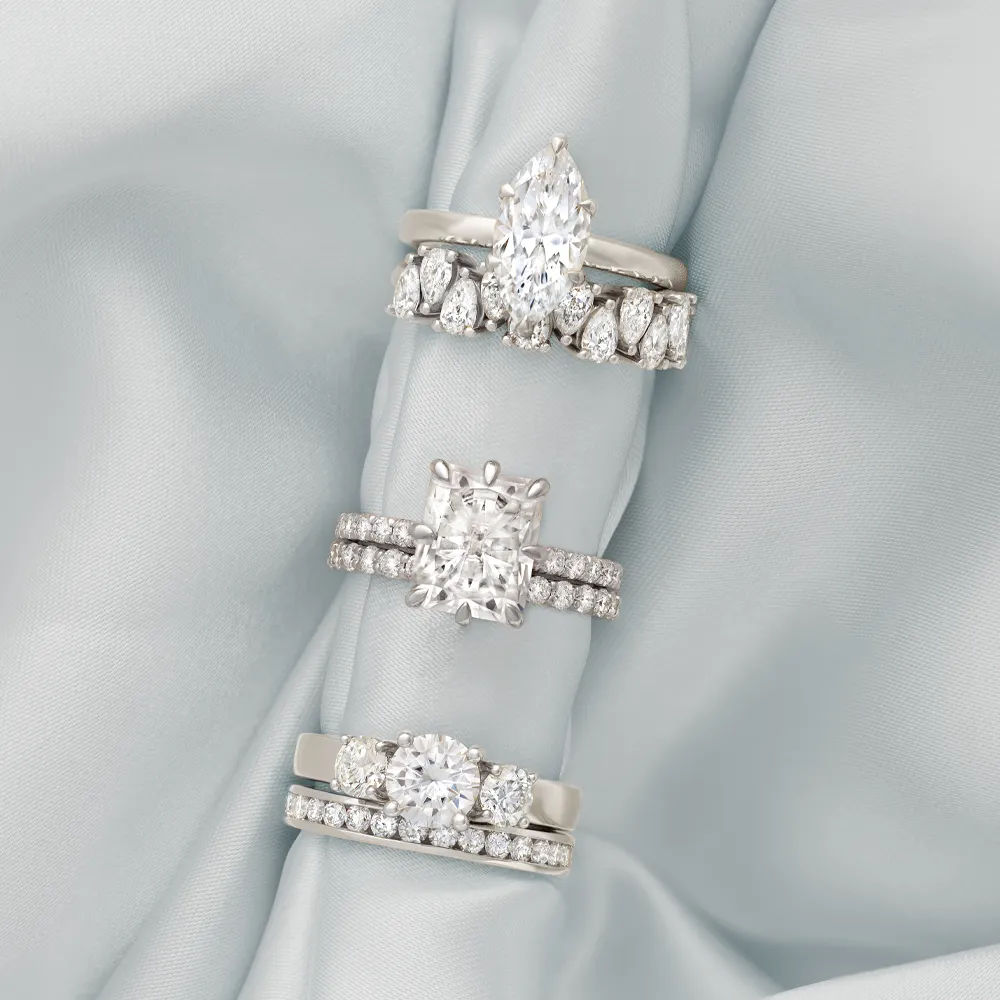 Three elegant diamond engagement rings displayed on soft fabric, showcasing various styles and settings.