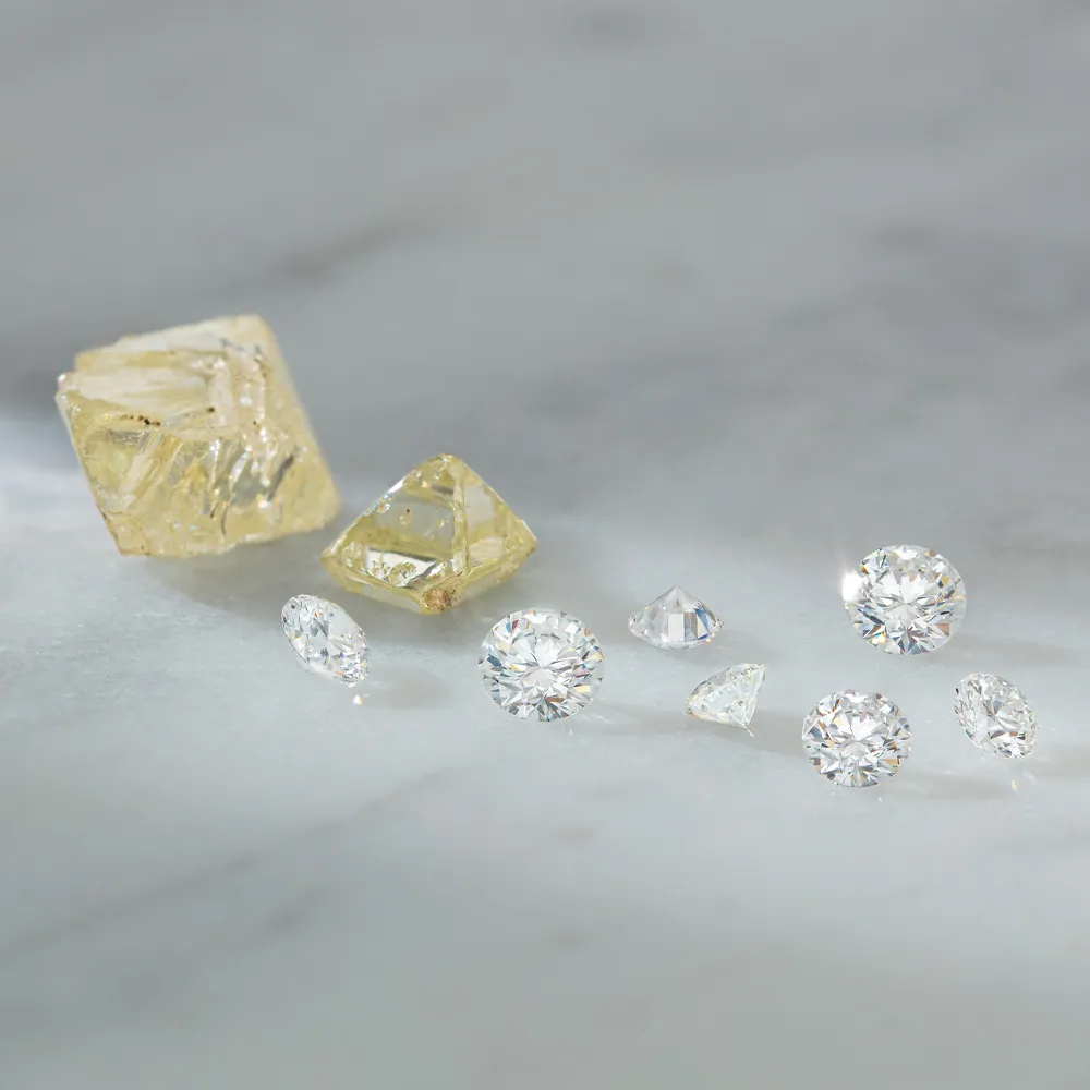 Various diamonds including round and fancy shapes, alongside yellow diamonds, displayed on a marble surface.