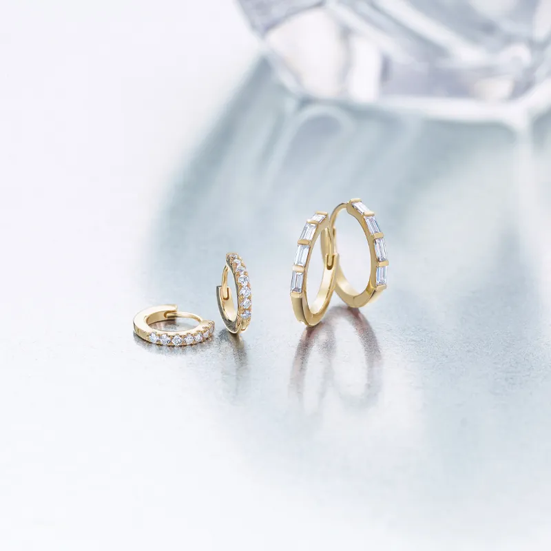 Two pairs of gold diamond earrings displayed on a reflective surface. Shop at Amos Jewelry in Wray for fine jewelry.