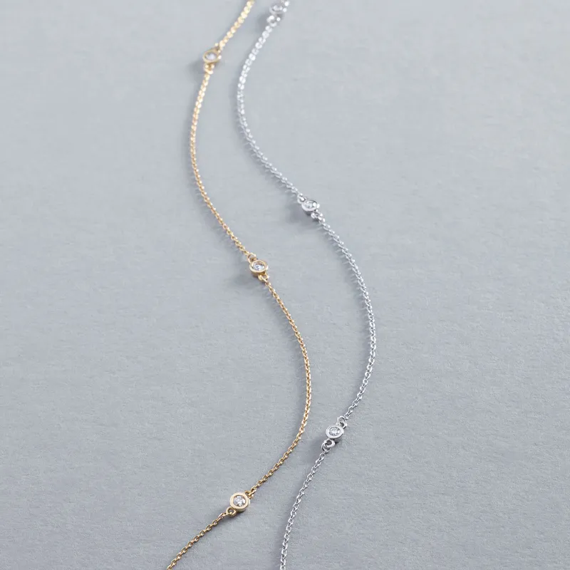 Two delicate diamond necklaces in gold and silver, elegantly displayed on a gray background.