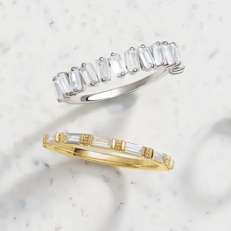Two elegant lab diamond fashion rings, one in silver and one in gold, displayed on a light marble background.