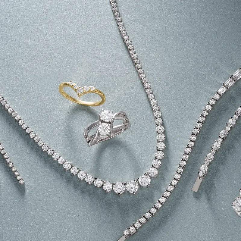 Elegant display of diamond jewelry including rings and necklaces on a soft gray background. Visit Amos Jewelry in Wray.