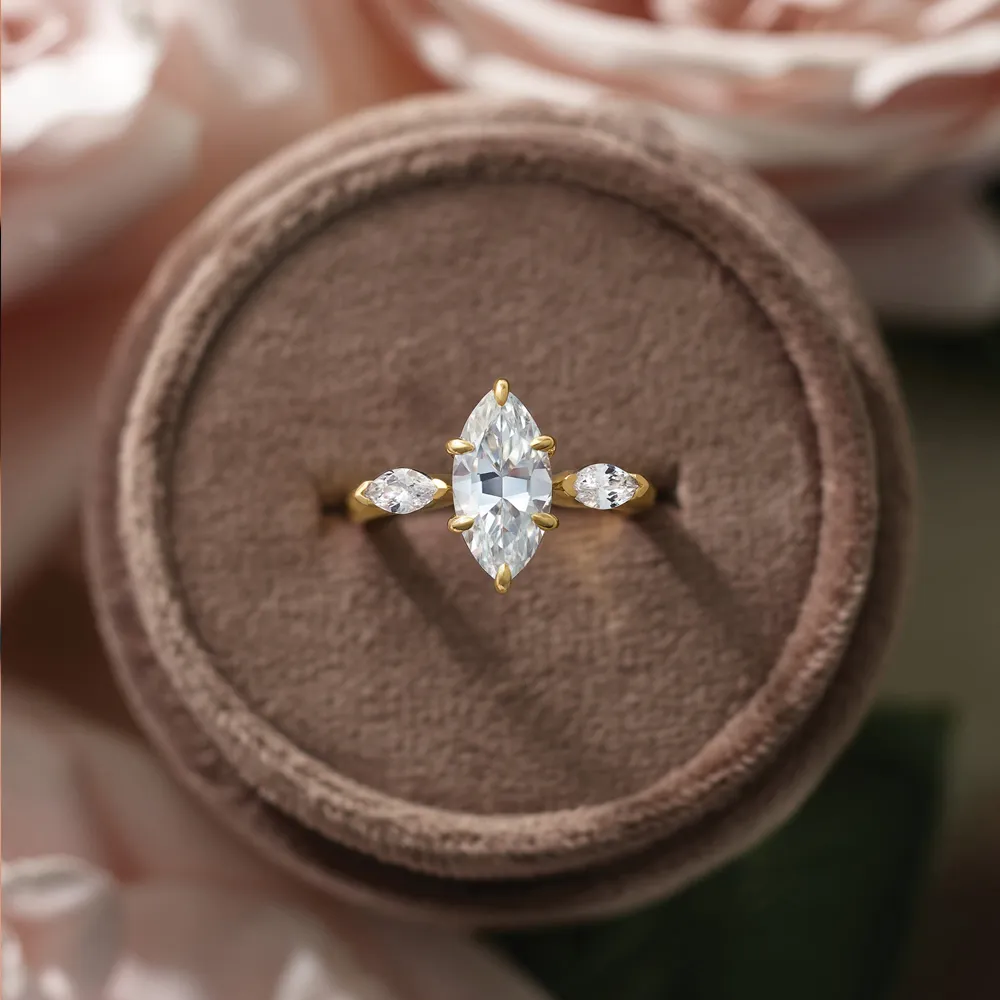 Elegant gold engagement ring with a marquise-cut center stone and two side diamonds, displayed on a velvet cushion.