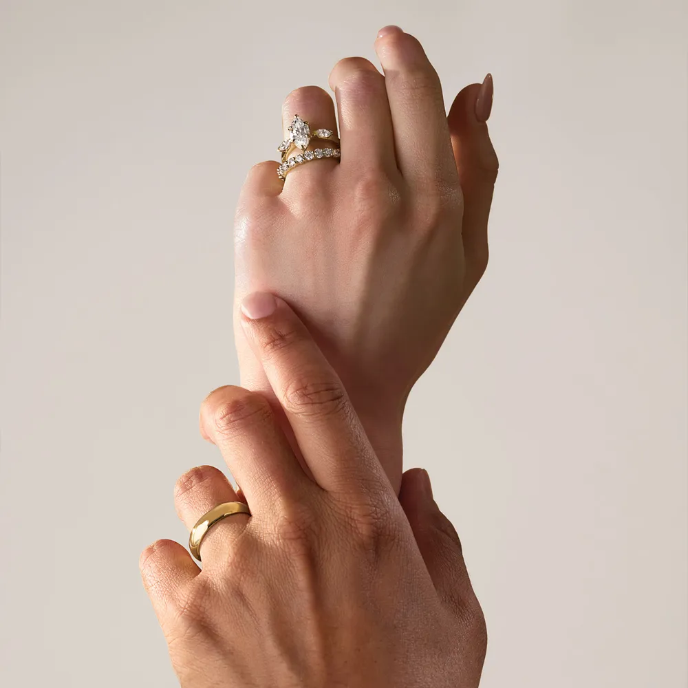Two hands with rings, one adorned with a diamond-studded band, gently touch each other. Explore engagement rings at Amos Jewelry