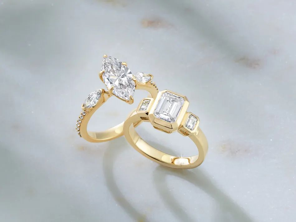 Two elegant gold engagement rings featuring diamonds, displayed on a marble surface.