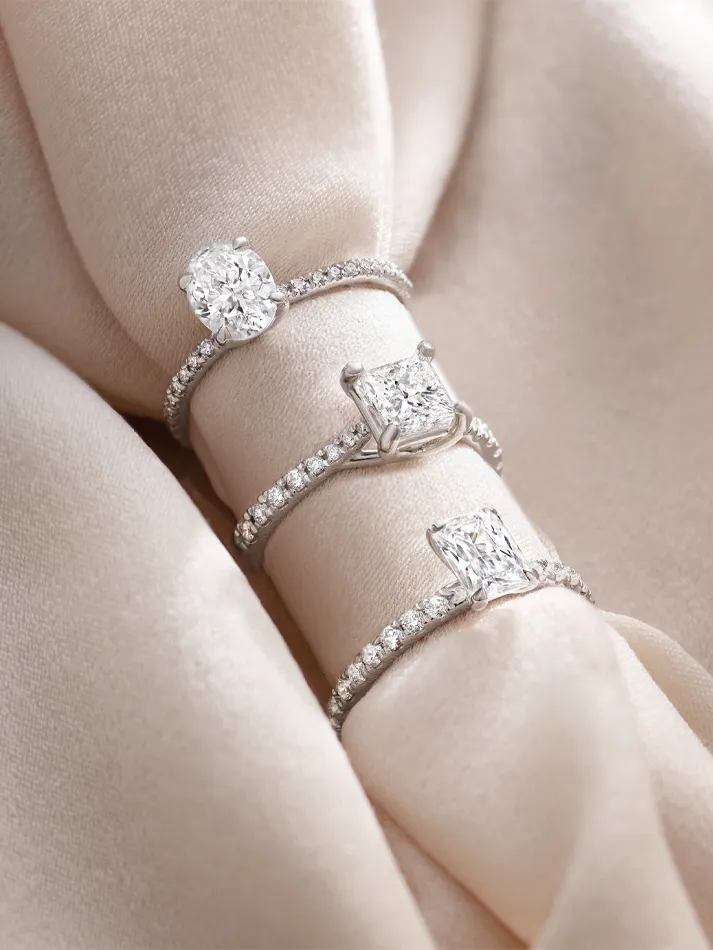 Three elegant diamond engagement rings displayed on soft fabric, showcasing their sparkling details. Visit Amos Jewelry in Wray.