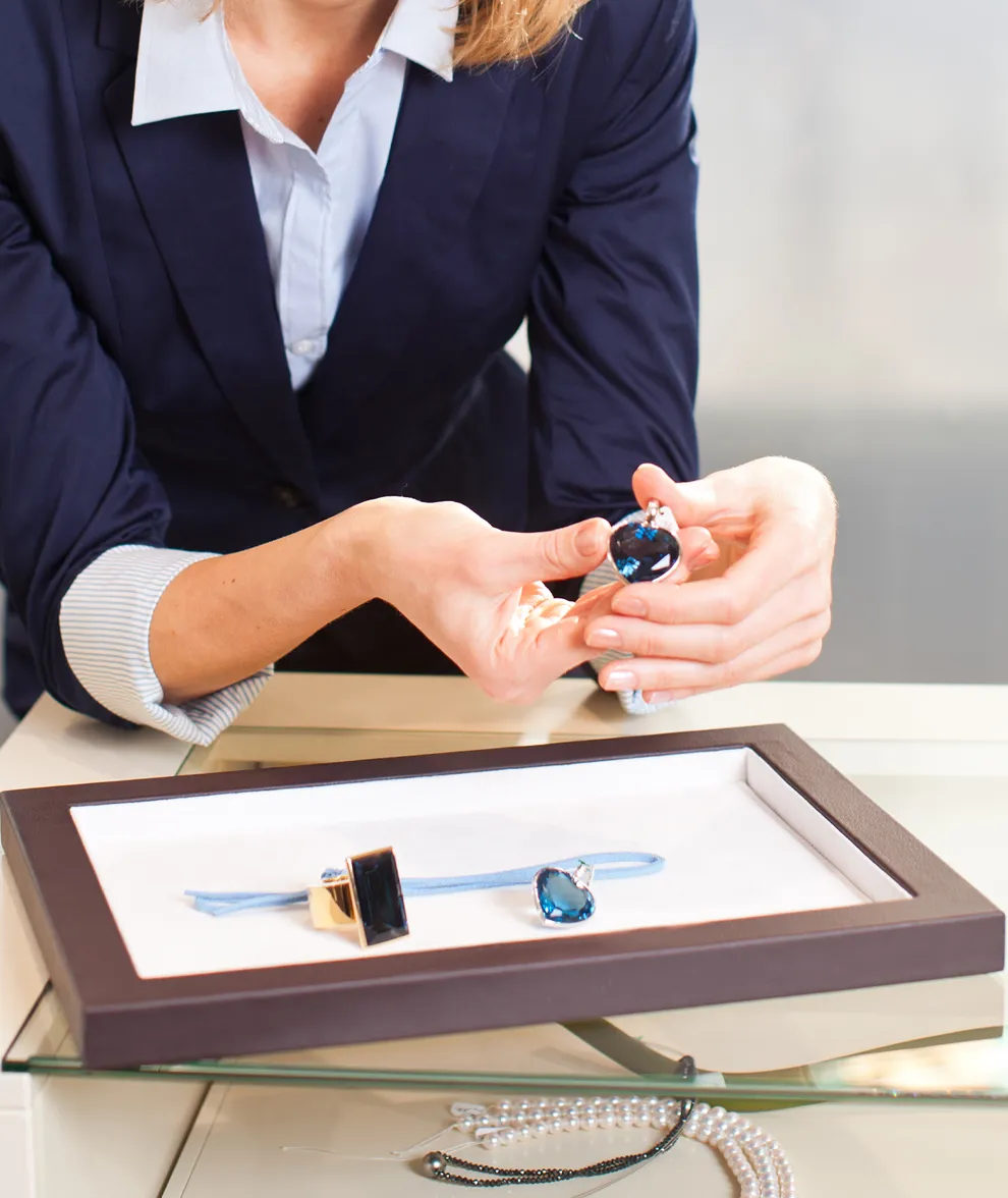 A woman in a suit showcases blue gemstone jewelry in a display case.