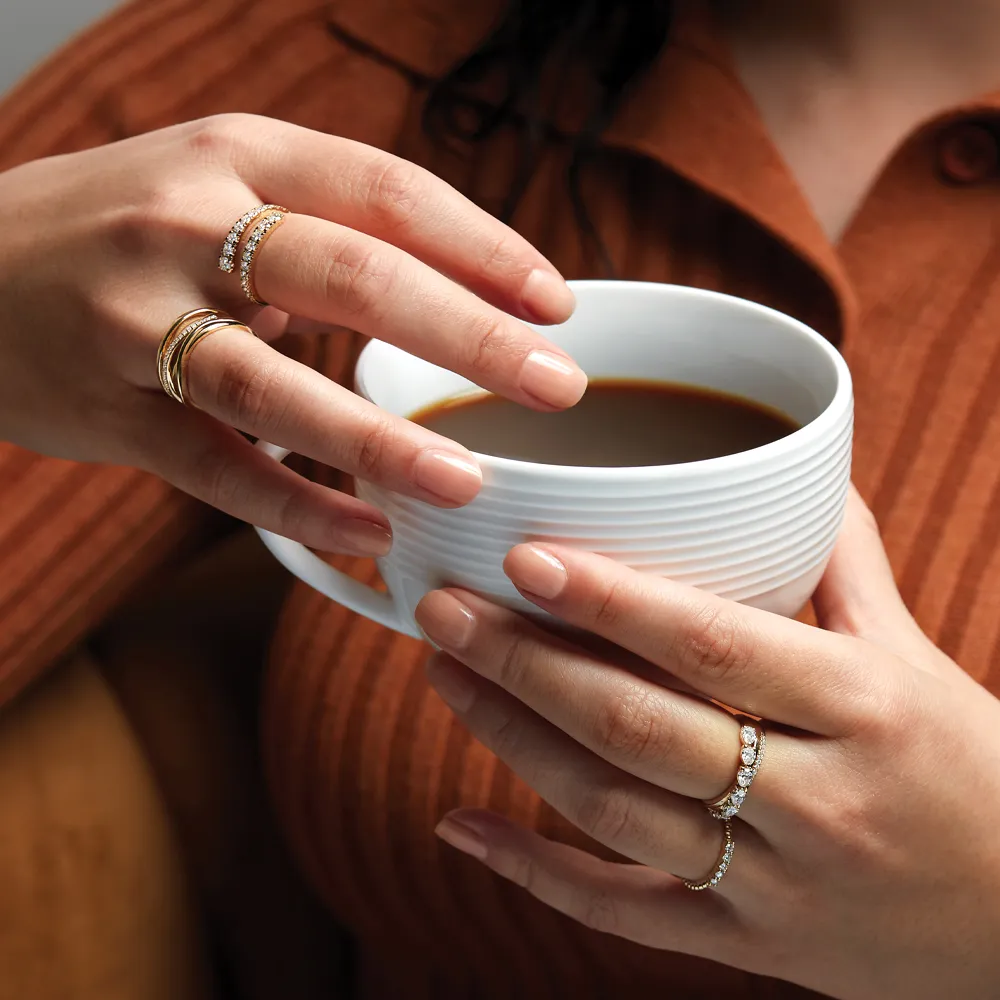 A woman holding a coffee cup, adorned with multiple gold rings, showcasing elegant jewelry from Amos Jewelry in Wray.