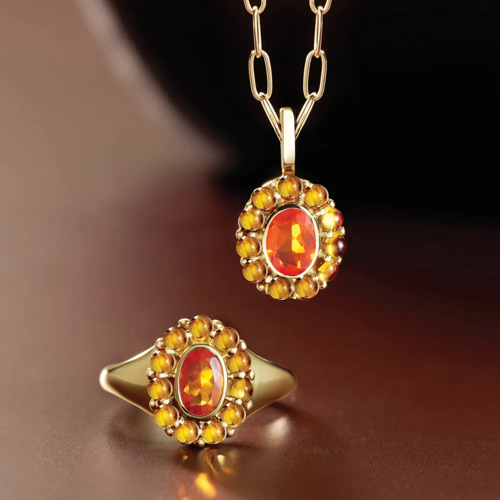Gold jewelry set featuring a ring and pendant with orange gemstones, displayed elegantly on a dark background.
