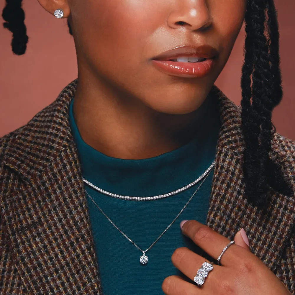Close-up of a woman wearing elegant jewelry: diamond earrings, layered necklaces, and rings.