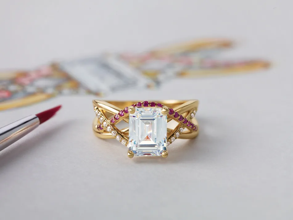 Elegant gold ring with a large emerald-cut center stone and ruby accents, displayed with a paintbrush nearby.