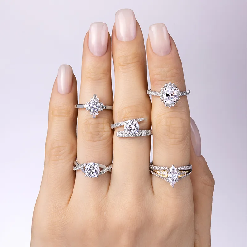 Five elegant engagement rings displayed on a hand with manicured nails against a light background.