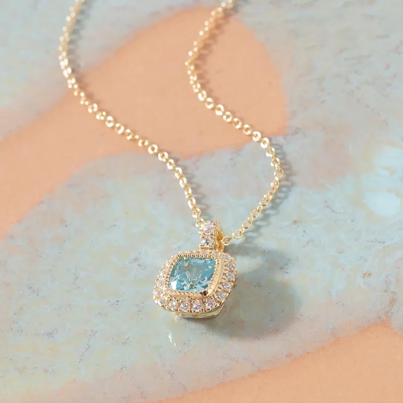 Gold necklace with a blue gemstone pendant surrounded by diamonds, displayed on a colorful background.