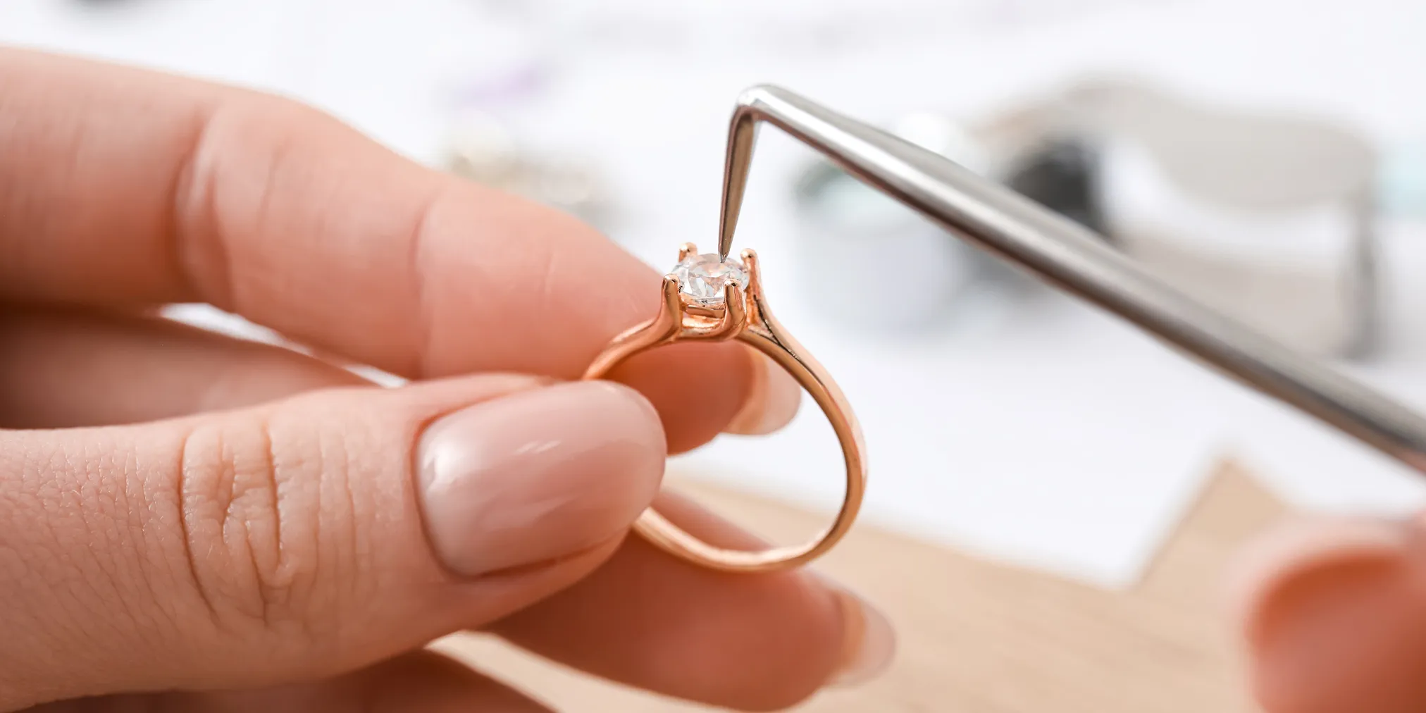 Close-up of a hand holding a rose gold engagement ring with a diamond, being adjusted with tweezers.