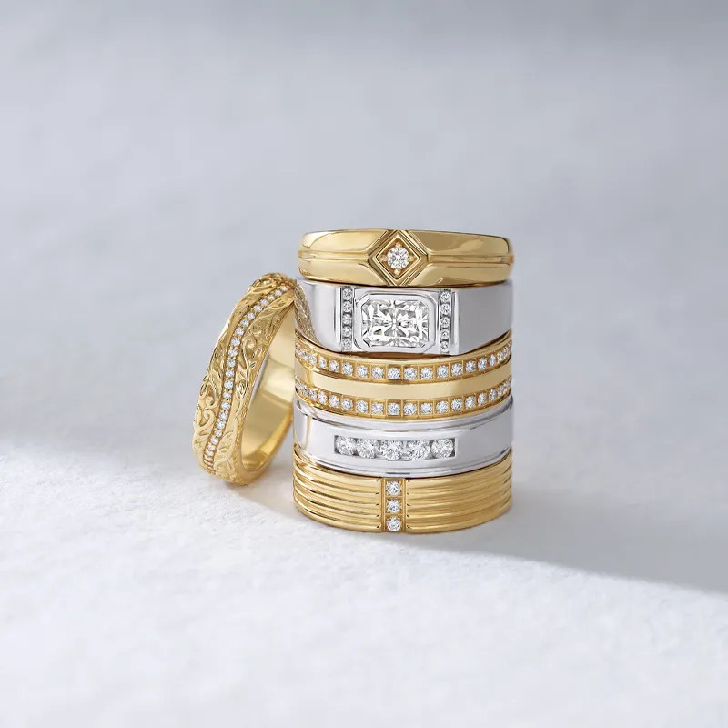 Stack of elegant wedding bands featuring gold and silver with diamonds, displayed on a soft background.