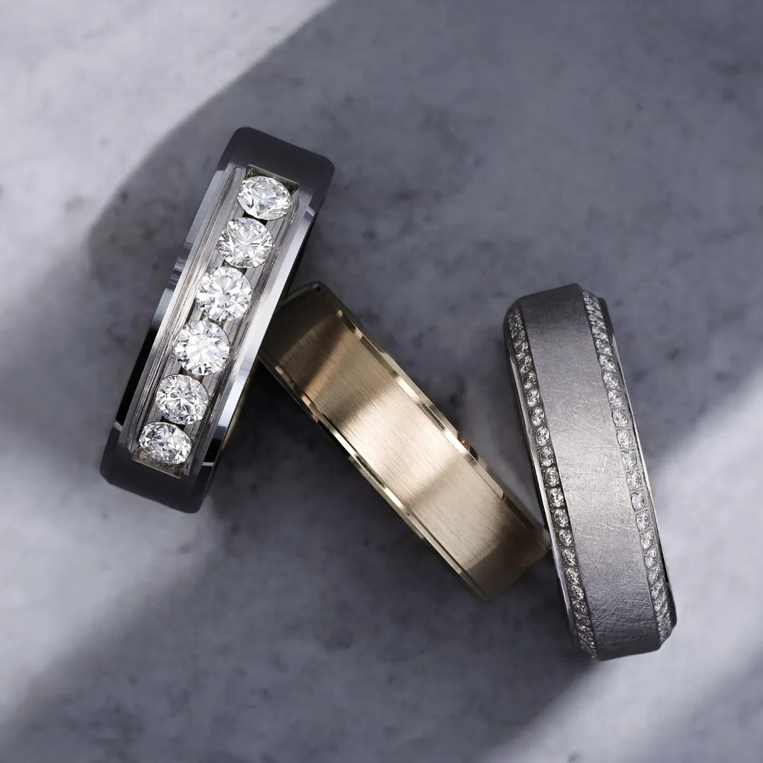 Three elegant wedding bands with diamonds on a marble surface.