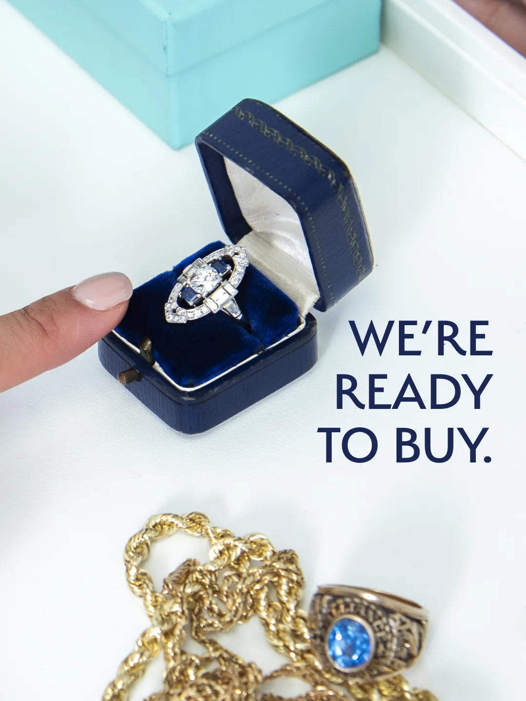 A finger points to a diamond ring in a blue box with gold jewelry nearby. Text reads 