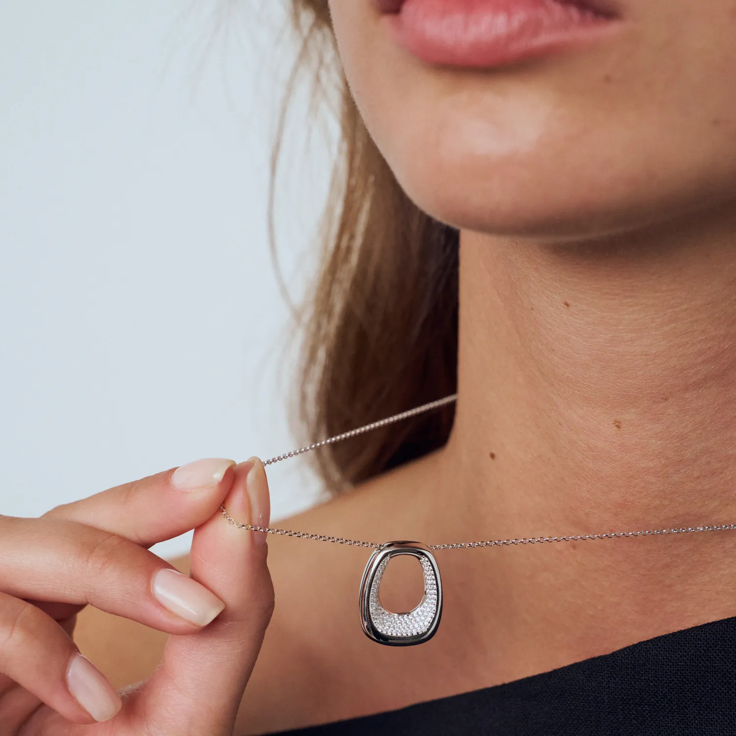 Woman holding a silver necklace with a sparkling pendant, promoting Arezzo Jewelers. Click to shop now.