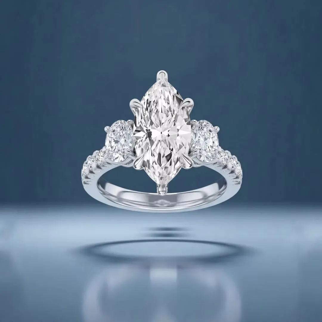 A centurion marquise-cut diamond ring with side stones on a reflective surface against a blue background.