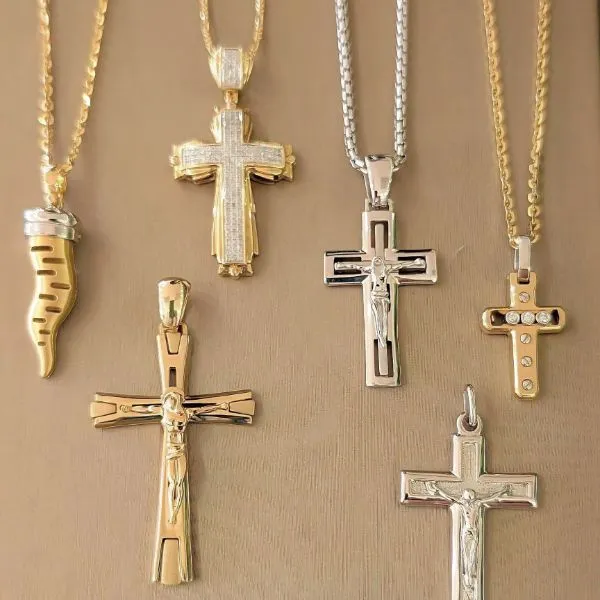 Three crucifix necklaces in gold, silver, and rose gold displayed on a white background. Shop at Arezzo Jewelers, Elmwood.