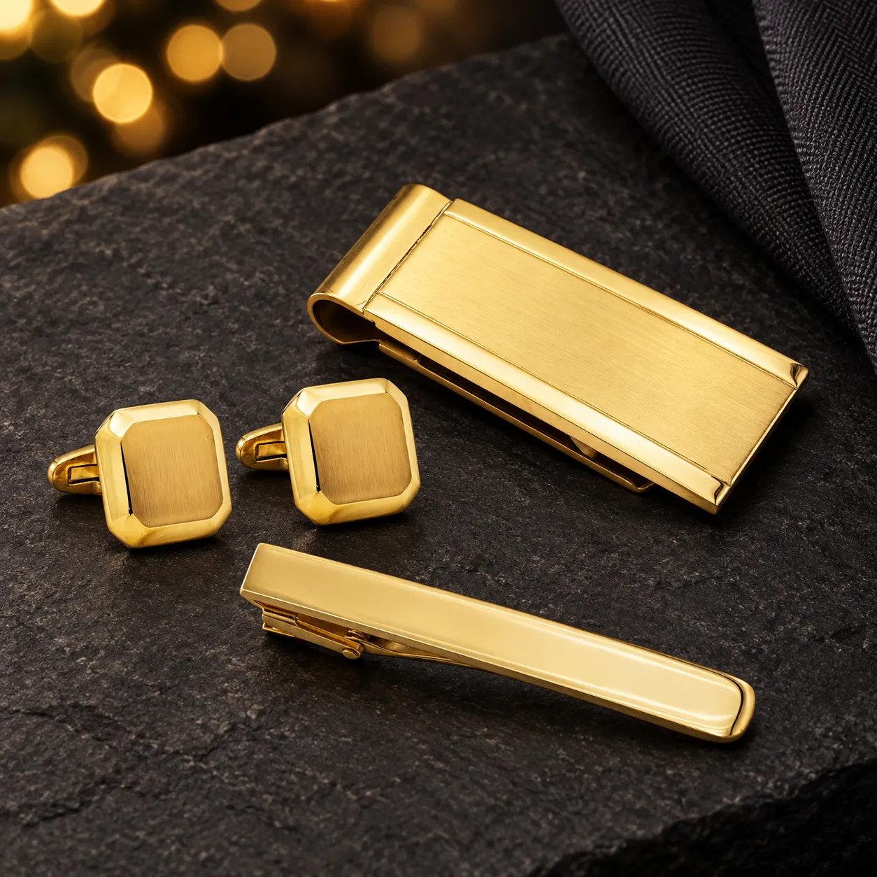 Gold-tone cufflinks, money clip and tie bar arranged on dark stone