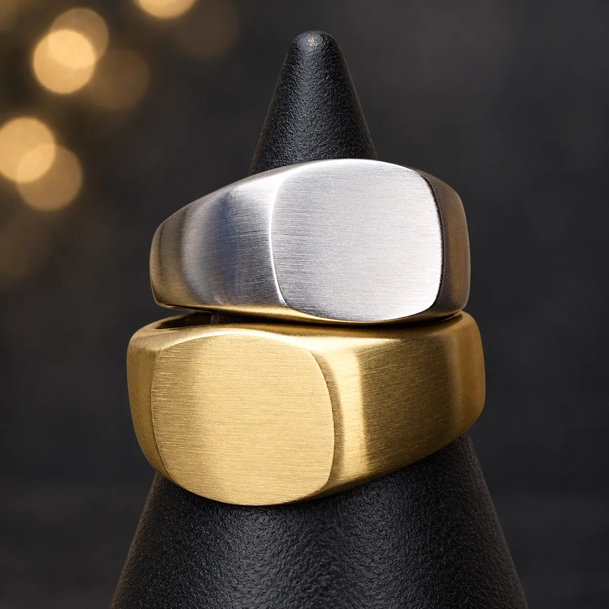 Silver-tone and gold-tone men's brushed signet rings on a dark display