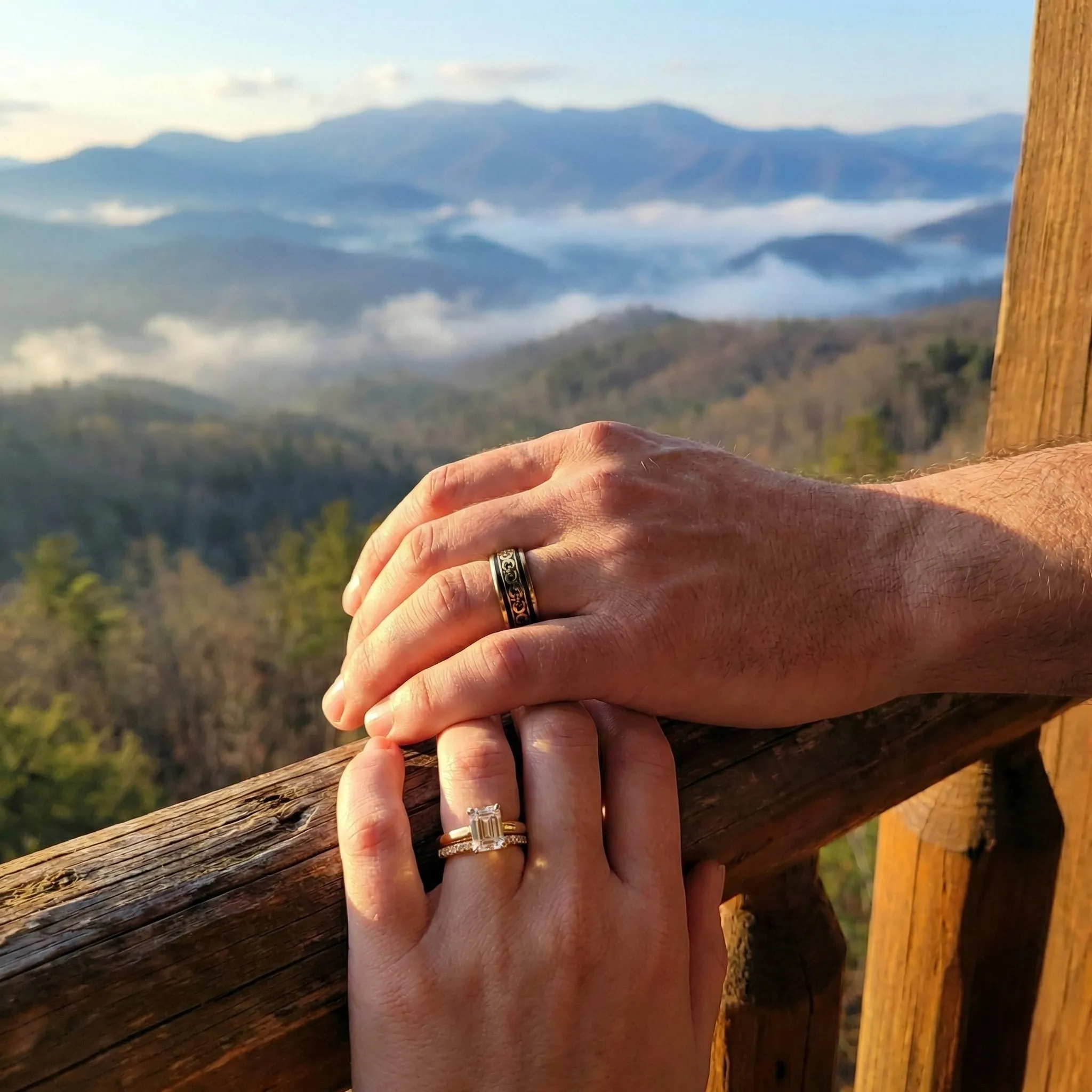 couple in yellow gold wedding sets clasping hands over a wooden railing overlooking the Appalachian mountains