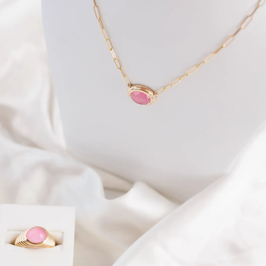 Gold necklace with pink stone pendant displayed on a bust, with a matching ring in a box beside it.