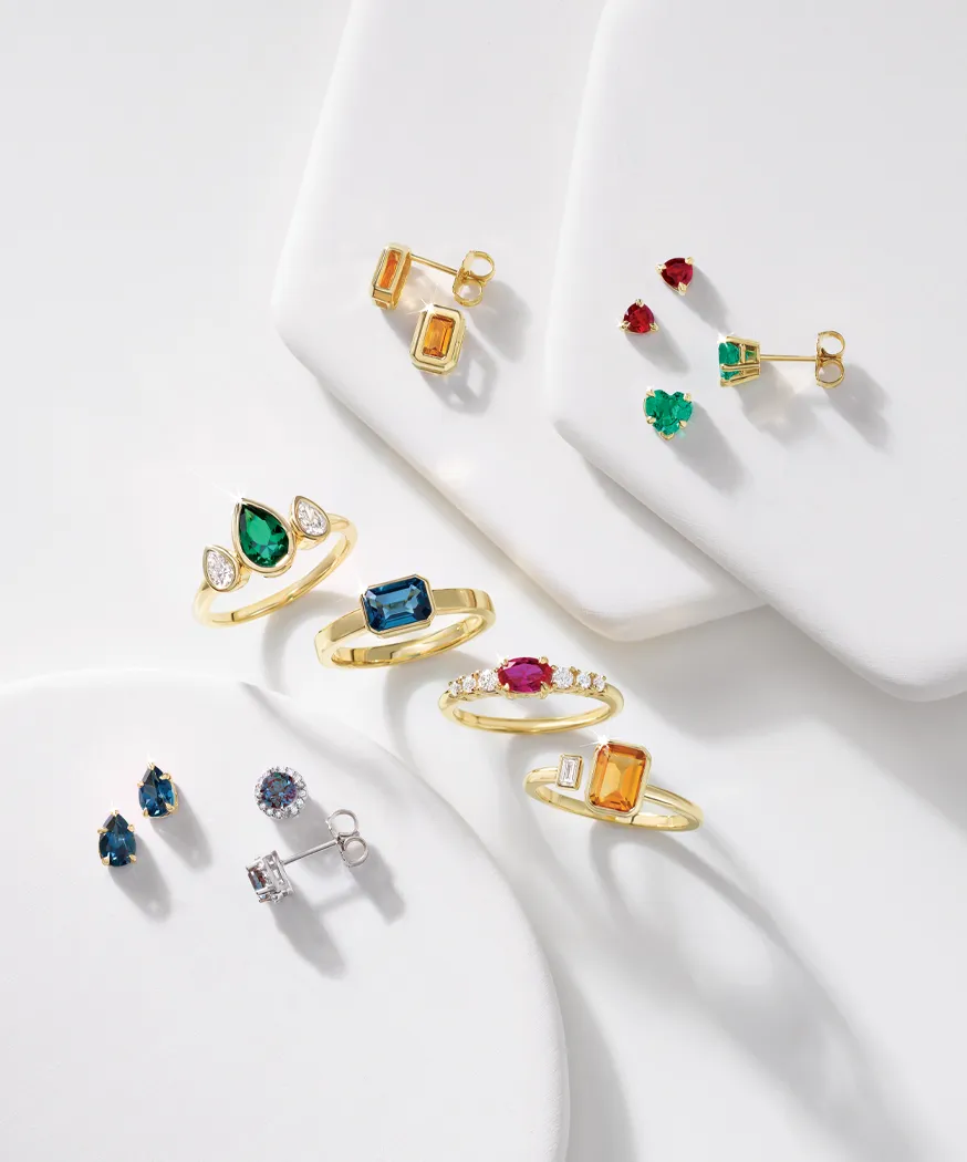 Colorful gold rings and earrings displayed on white surfaces, showcasing various gemstones.
