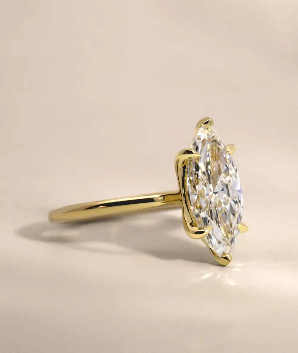 Elegant gold engagement ring featuring a marquise diamond, displayed on a soft background.