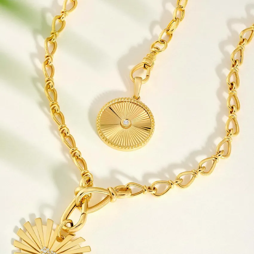 Gold pendant necklace with a sunburst design and diamond accent, displayed elegantly on a light background.