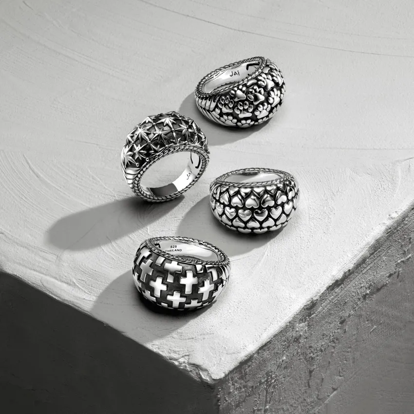 Four unique silver rings with intricate designs displayed on a textured surface.