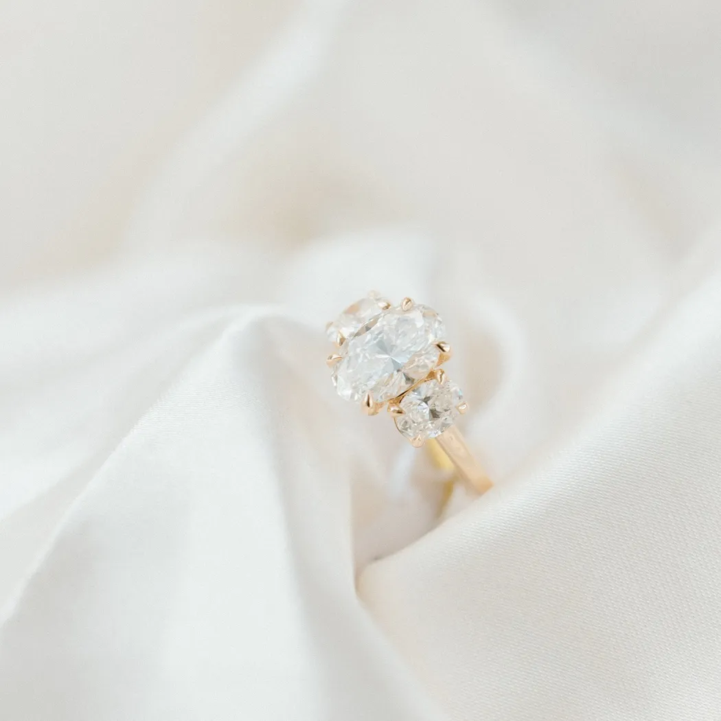 Elegant gold engagement ring with three sparkling diamonds on a soft satin background.