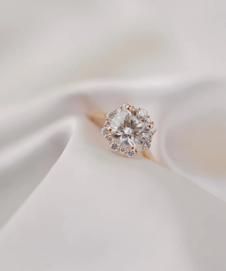 Elegant diamond engagement ring with a halo setting on soft satin fabric. Visit Barnes Jewelers in Goldsboro for more.