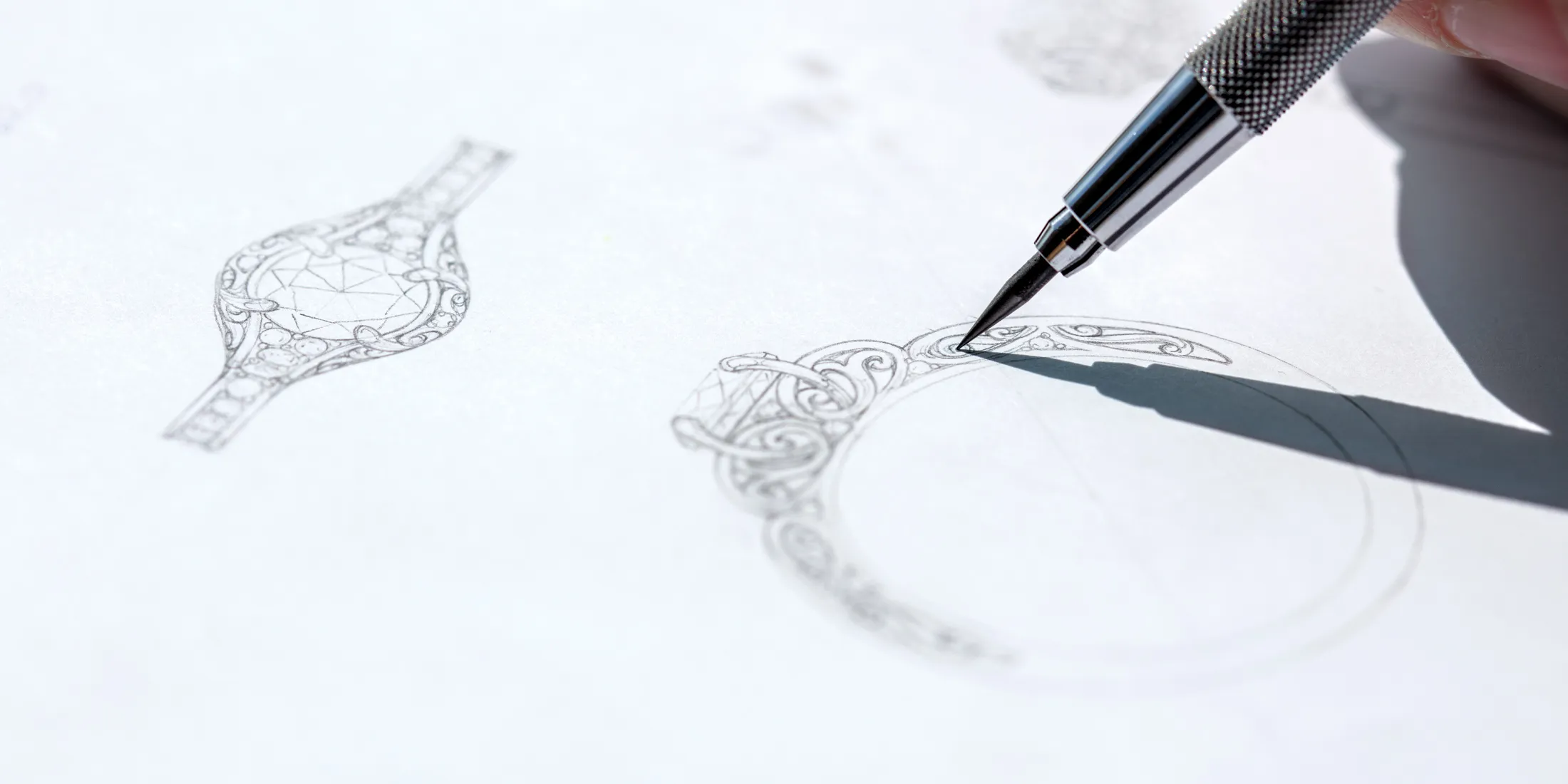A hand sketches an intricate ring design on paper, showcasing detailed patterns and a diamond shape.