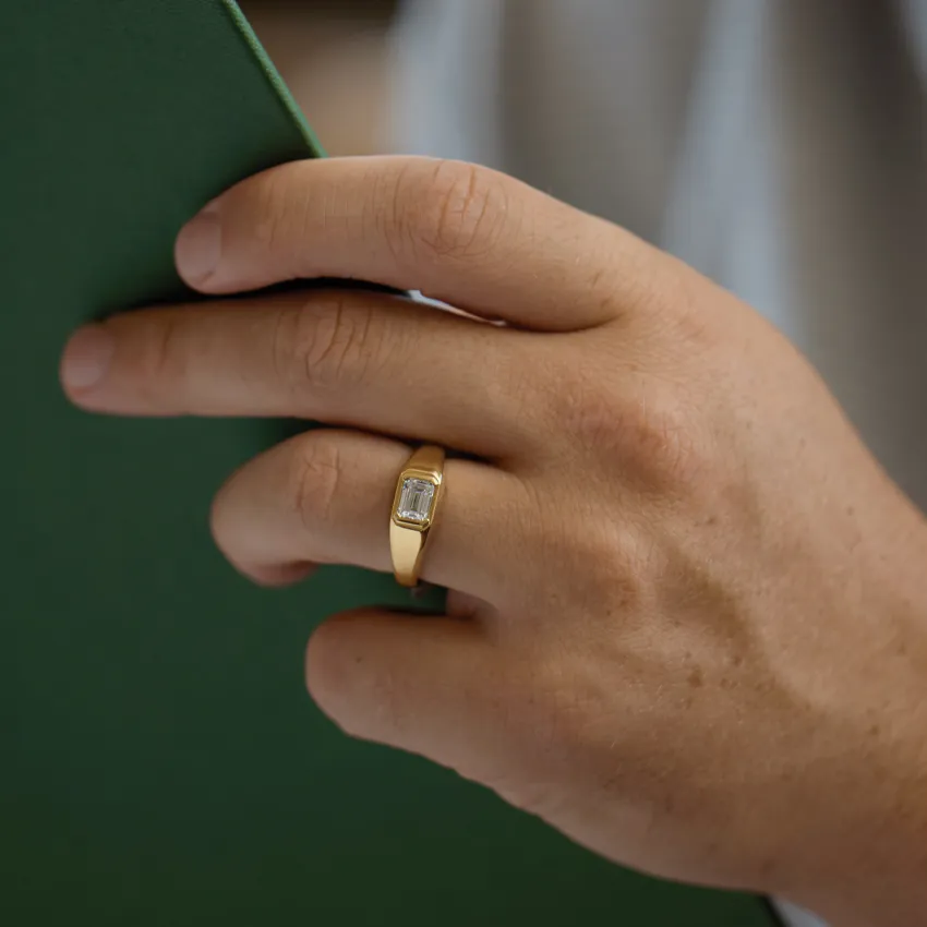 Close-up of a hand wearing a gold ring, holding a green book.