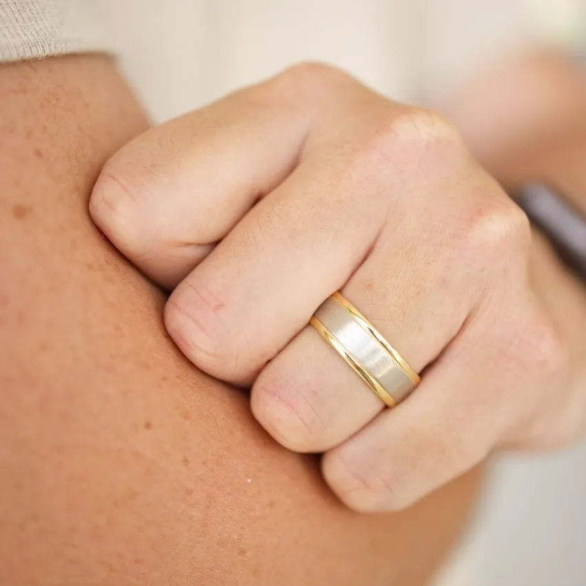 Close-up of a hand with a gold and silver men's wedding band, showcasing fine jewelry.