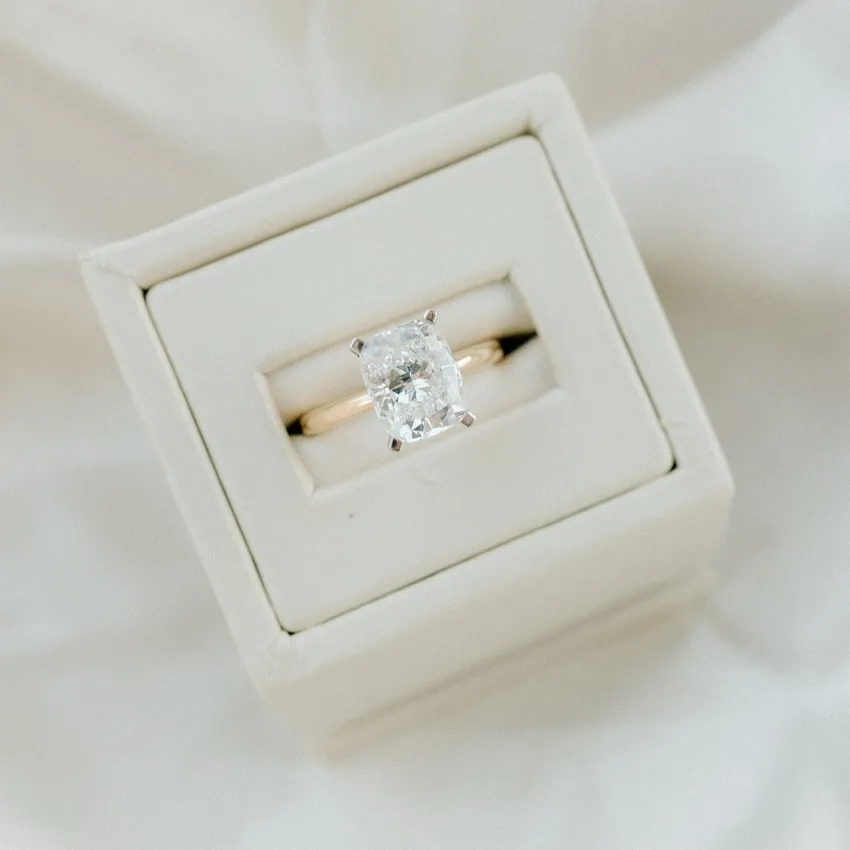 Elegant engagement ring with a rectangular diamond set in a gold band, displayed in a white box.