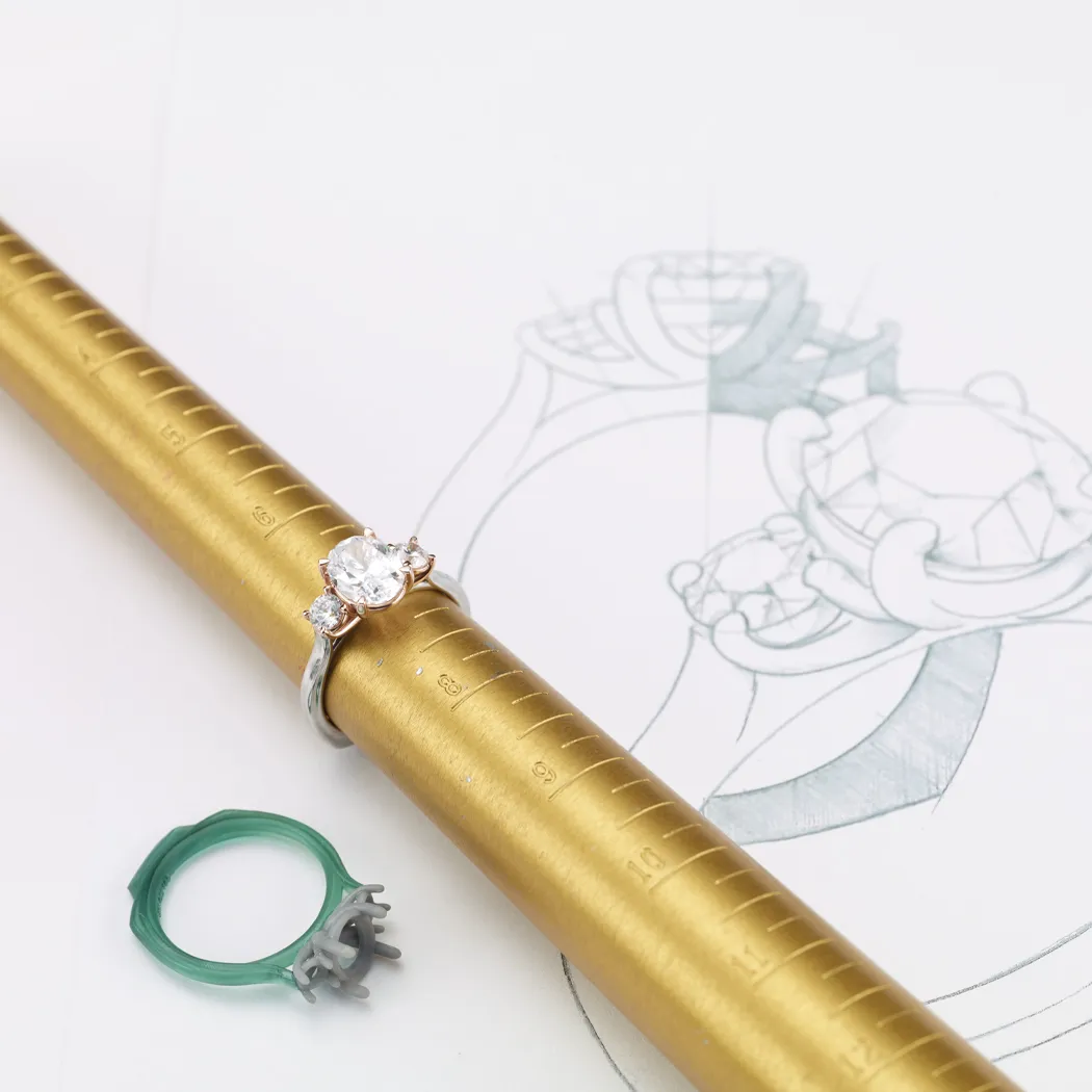 Engagement ring on a sizing mandrel with a design sketch in the background.