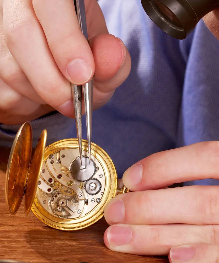 A jeweler repairs a vintage pocket watch using tweezers, showcasing intricate gears and craftsmanship.