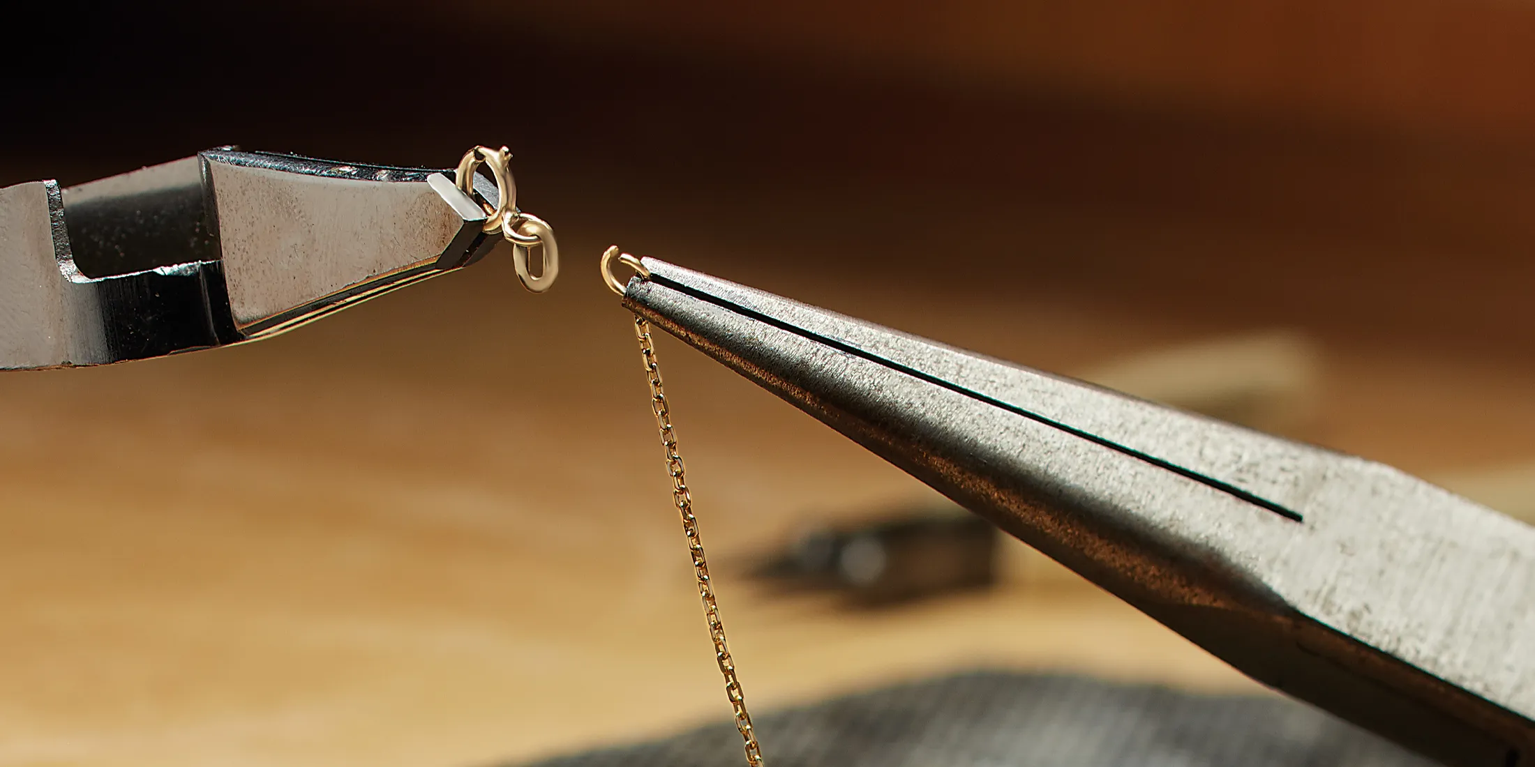 Close-up of pliers holding a gold chain link, showcasing jewelry crafting.