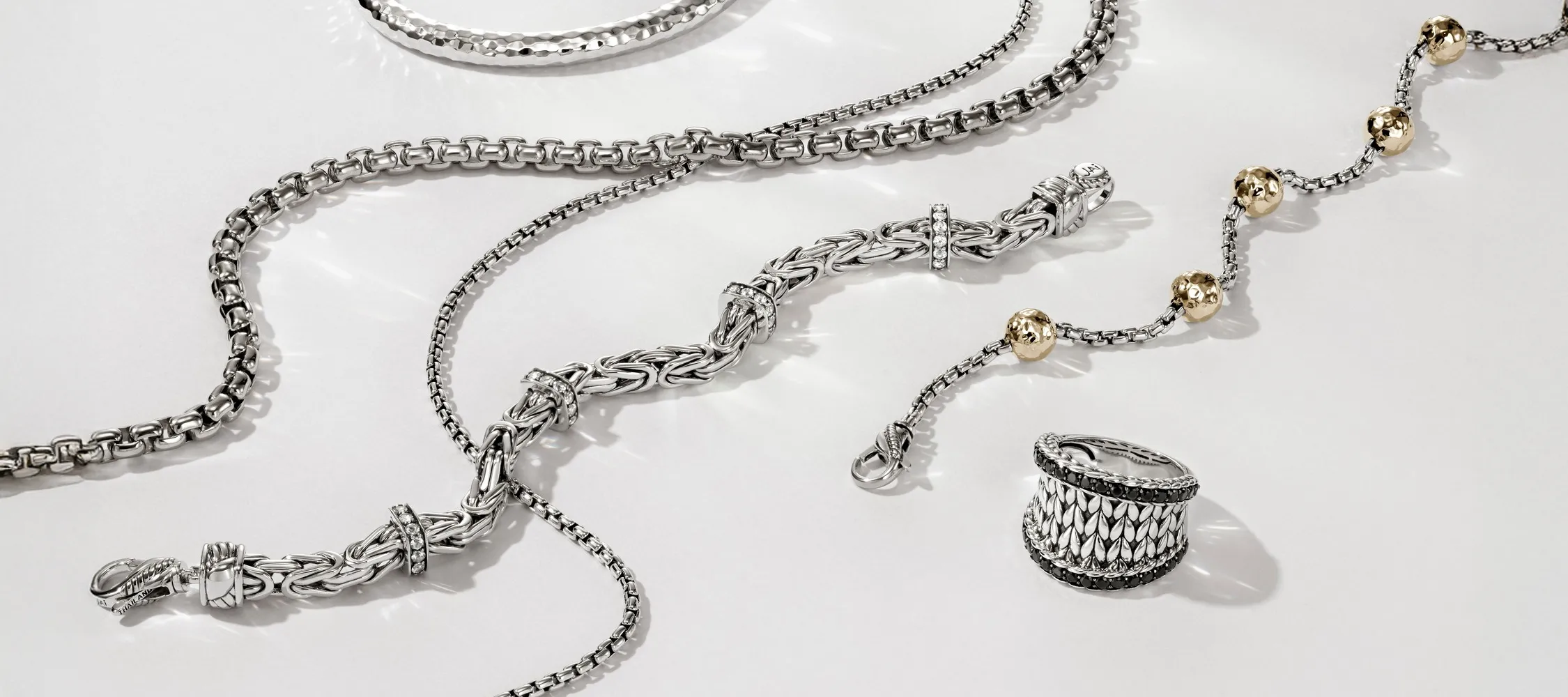 Silver jewelry pieces including chains and a ring, showcasing intricate designs and textures.