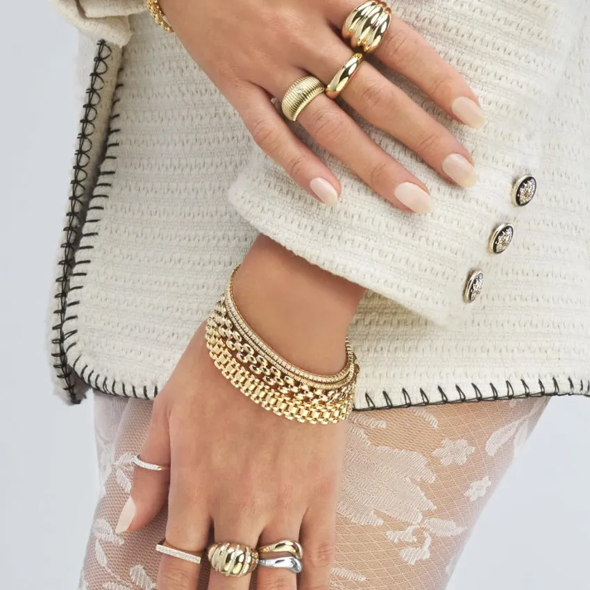 Close-up of hands adorned with various gold rings and bracelets, showcasing elegant jewelry styles.
