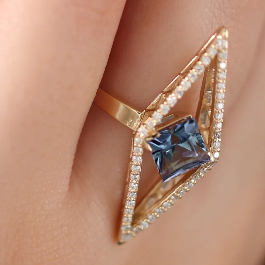 Elegant gold ring featuring a blue gemstone in a diamond-shaped setting, surrounded by small sparkling diamonds.