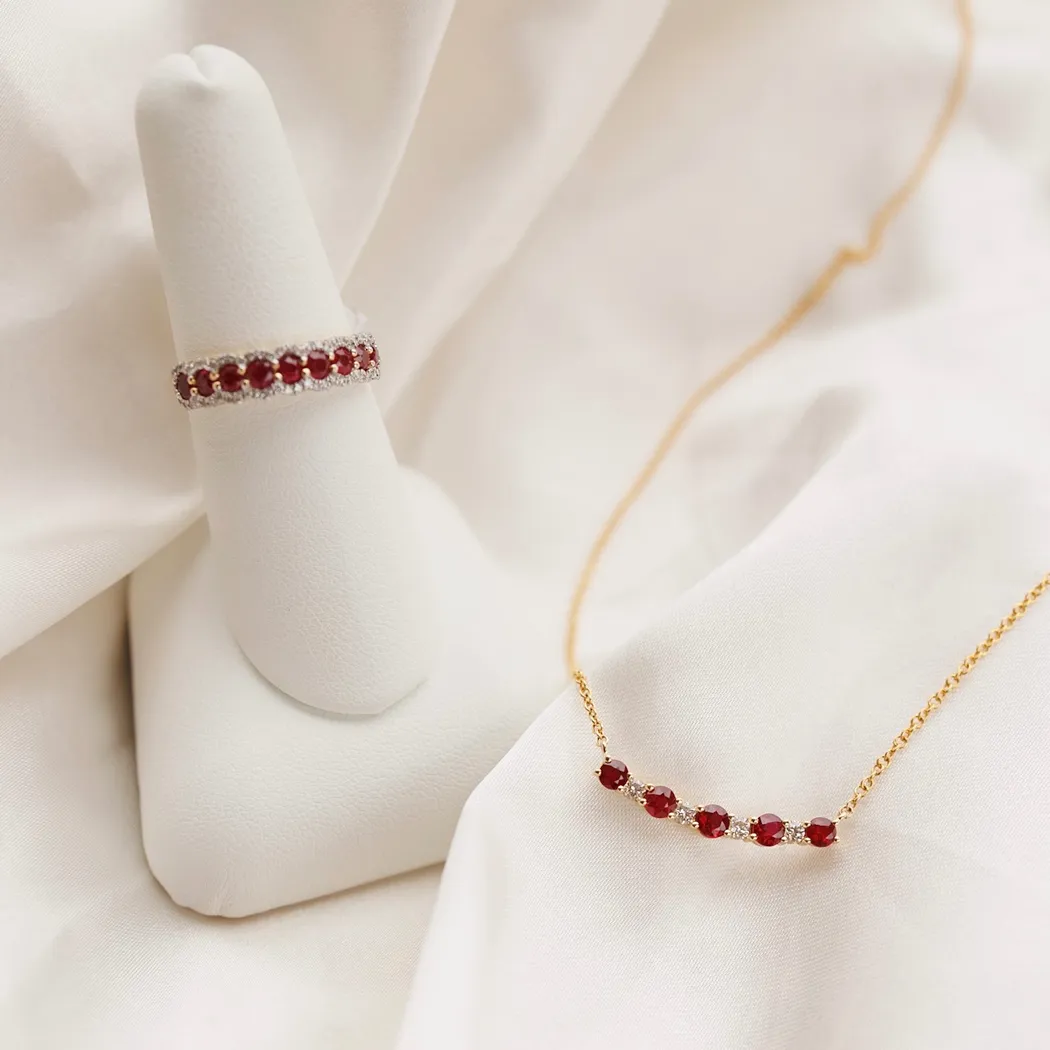 Elegant gold necklace and ring featuring red gemstones, displayed on a soft fabric background.